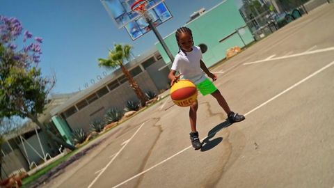 A kid dribbling a basketball on an outdoor court