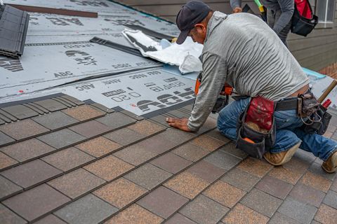 A roofer installing asphalt shingles on a house
