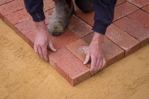 A worker laying brick pavers on sand