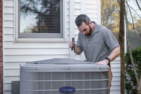 A technician servicing an outdoor air conditioning unit beside a house