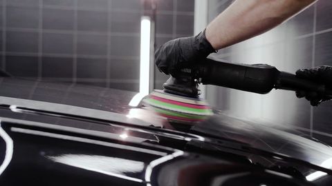 A detailer polishing a car with a machine buffer