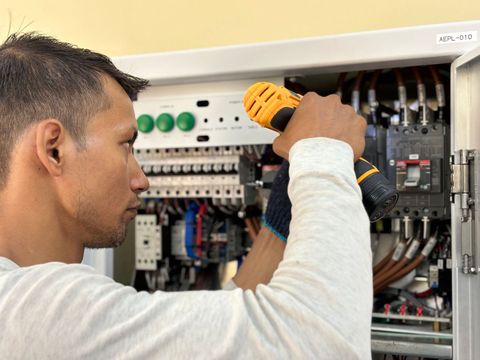 An electrician using a drill on an electrical panel