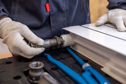A plumber in work gloves fitting pipes to a radiator