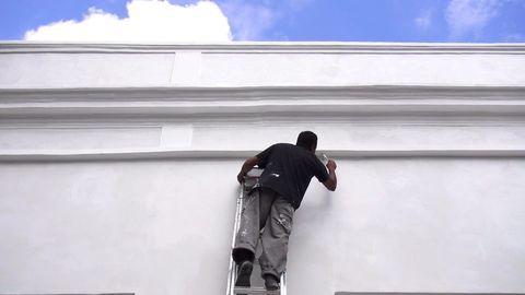 A painter on a ladder painting the outside of a building